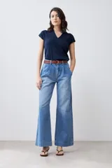 Pantalón de jean celeste de corte ancho, con cintura alta, pinzas y bolsillos laterales. Se ajusta a la cintura con un cinturón de cuero marrón.