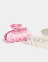 Set de dos broches para el pelo tipo pinza. Uno es de color blanco perlado con apliques de perlas sintéticas formando un moño. El otro es de color rosa con estampado de moños en rosa más oscuro.