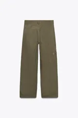 Pantalón cargo color verde oliva, de tiro alto y corte amplio. Presenta bolsillos de plastrón en pierna y espalda, trabillas en la cintura y cierre frontal con cremallera, botón interior y gancho metálico.