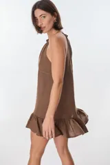 Vestido corto color beige, con escote halter, tirantes finos y falda con volados.