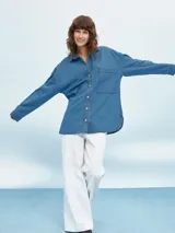 Camisa de jean celeste, de corte amplio, con cuello clásico, cierre frontal con botones y bolsillo de parche en el pecho.