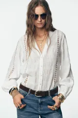 Blusa blanca de manga larga con escote en pico, detalle de tejido con frunces, entredoses y plumeti. Cierre frontal con botones.