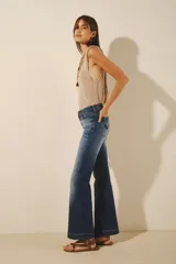 Jean de mujer color azul oscuro, tiro alto, corte oxford (o campana moderada) con desgaste localizado y bordado de alas negras en los bolsillos traseros.