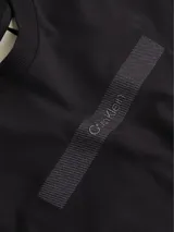 Remera negra de algodón con cuello redondo y manga corta. Presenta una barra horizontal texturizada con el logo de Calvin Klein en relieve en el pecho.