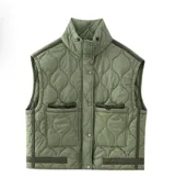 Chaleco acolchado verde oliva con cuello alto, cierre frontal con botones a presión y bolsillos delanteros con solapa y cordón ajustable. Ribete en contraste color marrón oscuro en hombros, sisas y ruedo.