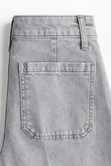 Pantalón de jean de tiro alto, color gris lavado, con pierna ancha y puños doblados. Presenta bolsillos de parche grandes en la parte delantera y bolsillos traseros.