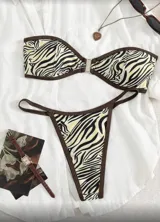 Conjunto de bikini con estampado de cebra en tonos beige y negro, con ribetes marrones. Incluye corpiño bandeau con hebilla metálica central y tanga de tiro bajo.