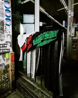 Pantalón deportivo gris jaspeado, estilo jogging, con corte ancho y tres franjas blancas verticales a lo largo de las piernas. Presenta un forro interior de tela escocesa roja y negra visible en la cintura.