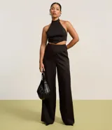 Pantalón de vestir negro de corte recto, sin cintura, con pinzas delanteras y cierre con cremallera y gancho.