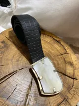 Cinto de cuero negro con textura tipo cocodrilo y hebilla rectangular de bronce con aplique de guampa.