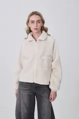 Campera de poliéster tipo sherpa en color natural, con diseño holgado, cuello alto y cierre frontal completo. Presenta un bolsillo de parche con cierre en el pecho y mangas largas con puños elásticos.