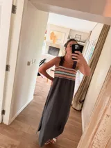 Vestido largo color gris oscuro, con tirantes anchos y un canesú con tejido de punto en tonos coral, turquesa y beige. El vestido tiene un corte holgado y una abertura lateral en la falda.