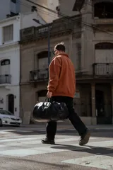 Bolso duffel negro de cuero sintético con logo de ancla bordado en rosa. Tiene doble asa de mano reforzada, correa de hombro regulable y desmontable, cierre superior con doble cremallera y tres bolsillos (dos exteriores y uno interior).