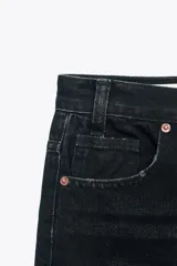 Pantalón de jean celeste de tiro alto, corte wide leg y largo hasta el tobillo. Presenta un diseño asimétrico en la cintura con cierre frontal cruzado con cremallera y botones metálicos.