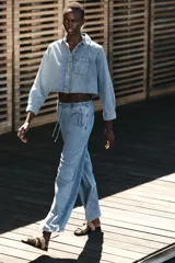 Camisa corta de denim celeste, con cuello solapa, manga larga, bolsillo delantero de plastrón y cierre frontal con botones metálicos.