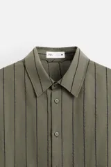 Camisa de hombre regular fit, color blanco con rayas verticales negras, cuello solapa, manga larga con puños abotonados y cierre frontal con botones.