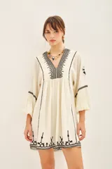 Vestido corto negro con bordado de hilo blanco, escote en V y mangas largas abullonadas.