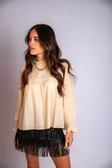 Camisa color crema con cuello alto y mangas largas con volados en los puños. Presenta detalles de crochet y broderie en el frente.