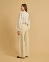 Pantalón acampanado color beige con pinzas, bolsillos italianos y bolsillos de parche con solapas en los laterales. Cierre con botones y cintura con trabillas.