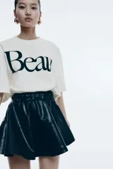 Remera cropped color crudo de corte holgado con cuello redondo acanalado, hombros caídos y bajo recto. Estampado frontal con la palabra 'Beau' en color negro.