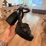 Sandalias negras de cuero sintético con plataforma y taco cuadrado alto. Tiras cruzadas en el empeine y pulsera con hebilla al tobillo.