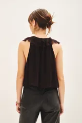 Blusa negra sin mangas, con escote en V profundo y volados en el frente. Tiene lazos en el cuello y gancho invisible para regular el escote.