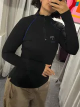 Remera térmica negra de manga larga con cierre frontal parcial, vivos en contraste color azul y logo bordado.