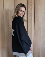 Buzo negro de punto con cuello redondo y manga larga. Tiene una estrella blanca estampada en la espalda y ribetes en color beige en cuello, puños y ruedo.