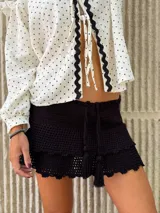 Mini falda negra tejida a crochet con volados y cordón ajustable con borlas.