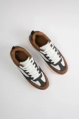 Zapatillas urbanas con exterior de cuero sintético color marrón, blanco y azul marino. Cordones blancos y suela de goma color caramelo.