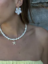 Gargantilla de cuentas blancas con dije de estrella de mar dorada.