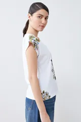 Remera blanca de algodón con escote en V y estampado floral en el frente y los hombros.
