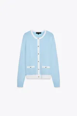 Chaqueta celeste de punto con cuello redondo y manga larga. Tiene cierre frontal con botones y detalle de falsos bolsillos delanteros con ribete blanco.