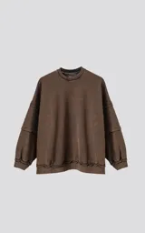 Buzo marrón de corte holgado con cuello redondo y mangas largas. Presenta detalles de costuras reforzadas en hombros y puños, y terminaciones desflecadas en ruedo y puños.
