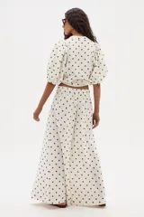 Pantalón de lino color crudo con lunares marrones, de corte ancho y tiro medio-alto, con elástico en la parte trasera de la cintura.