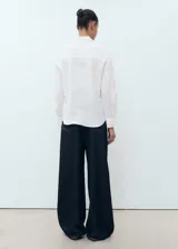 Camisa blanca de lino 100%, con diseño recto, cuello camisero, manga larga con puños abotonados y bolsillo de parche en el pecho.