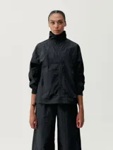 Chaqueta cortaviento negra de tejido técnico Wind_S con cuello alto, cierre frontal con cremallera, bolsillos laterales con cremallera y reguladores en el bajo.