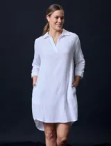 Vestido camisero blanco de algodón con cuello solapa, escote en V y mangas 3/4 regulables. Presenta bolsillos laterales verticales y abertura con botones en la espalda.