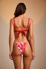 Top de bikini triangular con estampado de hojas rojas y rosadas sobre fondo blanco.