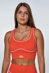 Conjunto deportivo naranja con costuras blancas, compuesto por un top con logo 'bk.' y un short de tiro alto.