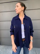 Camisa azul marino de tejido de punto en algodón, con cuello camisero, cierre frontal con botones dorados, bolsillo de parche con solapa de cuero sintético y mangas largas.