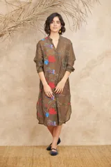 Vestido camisero midi color marrón translúcido, con cuello en V, mangas largas y cierre frontal con botones. Presenta bordados de motivos marinos en tonos rojos, azules y blancos.