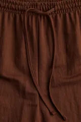 Pantalón marrón de punto, corte holgado, tiro alto, cintura elástica con cordón ajustable y perneras anchas.