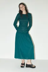 Vestido midi color verde esmeralda con textura plisada en la parte superior y falda lisa. Tiene cuello redondo y mangas largas.