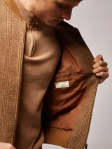 Campera bomber marrón con estampado a cuadros, cuello, puños y ruedo acanalados. Cierre frontal con cremallera.