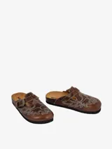 Mules de cuero color marrón con diseño vaquero, costuras decorativas con forma de águila y hebilla lateral ajustable.