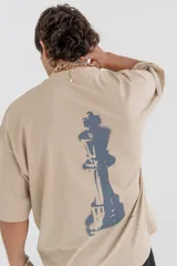 Remera color beige con estampado de una pieza de ajedrez en color naranja en la espalda.