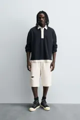 Polo negro de corte relaxed fit confeccionado en tejido con algodón. Cuello solapa con cierre frontal de botonadura. Manga larga. Bajo con aberturas laterales. Acabados en rib.