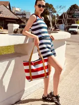 Bolso tipo tote rayado en rojo y blanco, con asas de cuero marrón.
