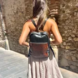 Mochila de cuero natural color negro con base marrón con textura de piel de cocodrilo. Tiene cuatro compartimentos independientes con cierre, dos bolsillos internos y correas de cuero regulables.
